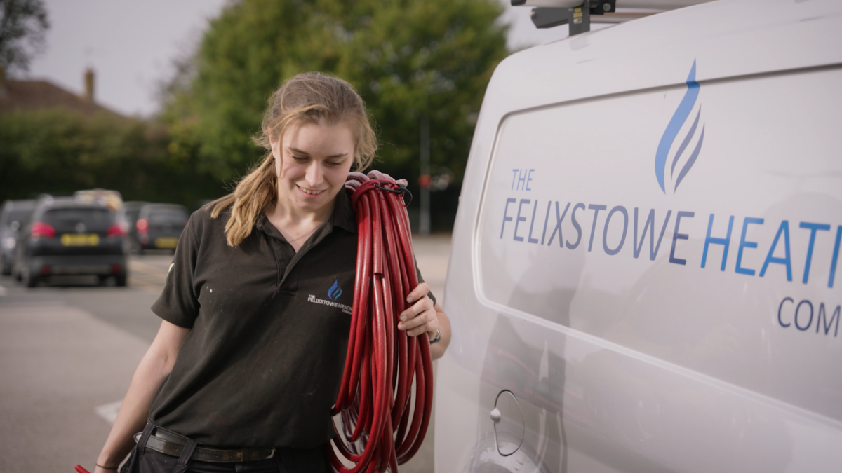 A young lady, who is a gas and heating engineer, carries a red hose past a Felixstowe Heating van