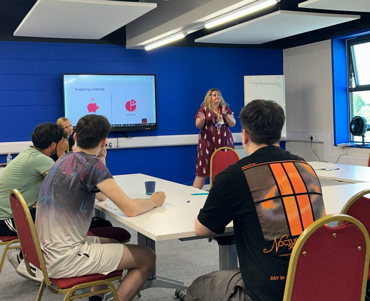 A Youth Employment Service group of students sit in an Inspire classroom at desks, listening to a presenter who is showing slides on a digital whiteboard.