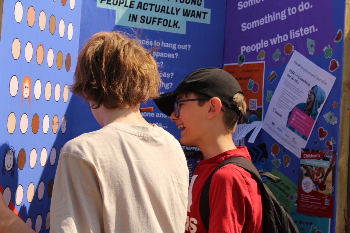 Two young people laugh as they look at self-portraits on an Inspire graffiti wall