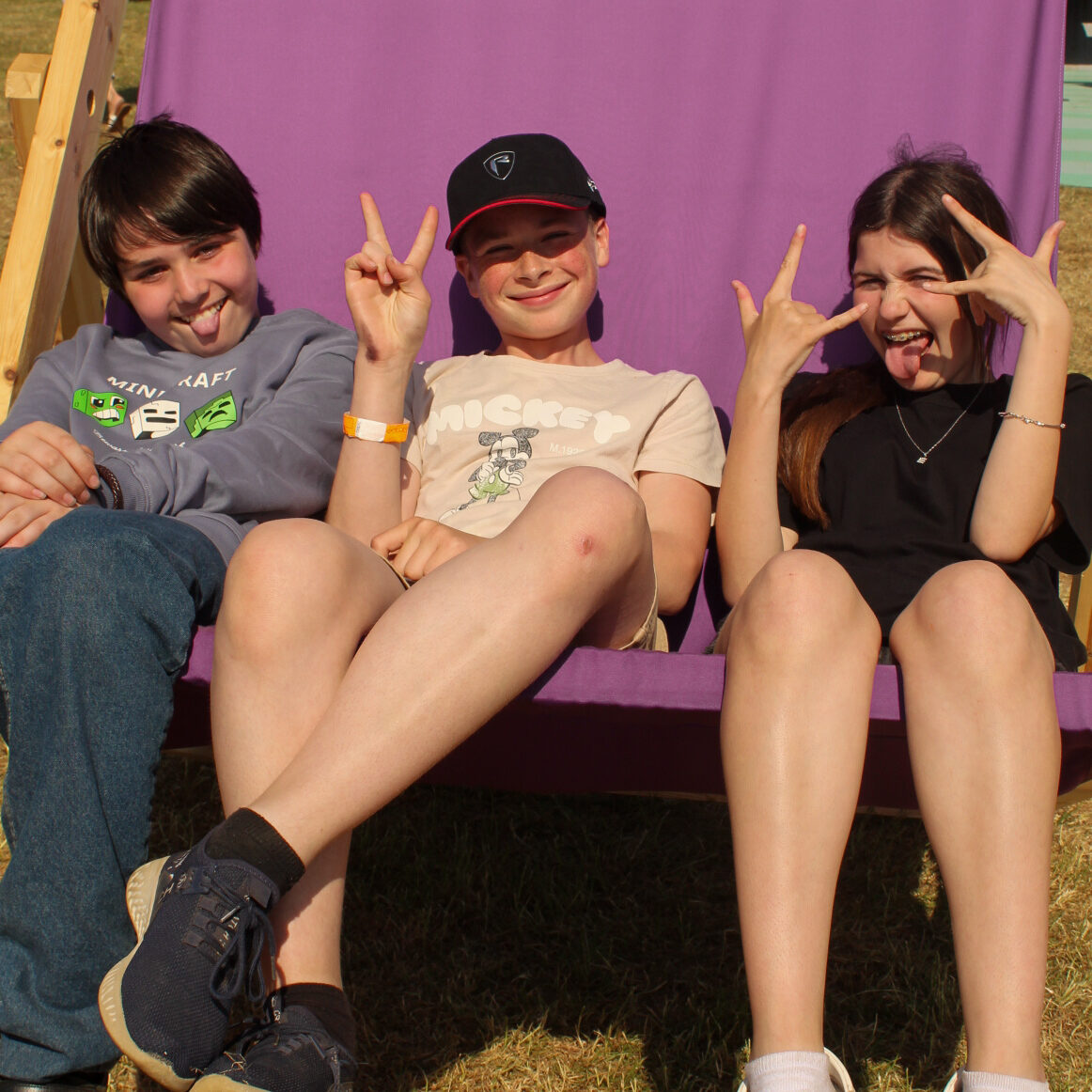 Three young people chilling out in an oversized purple deck chair, posing for the camera