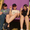 Three young people chilling out in an oversized purple deck chair, posing for the camera